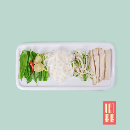 Vietnamese rice noodle dish with sliced chicken, fresh herbs, and lime on a white platter