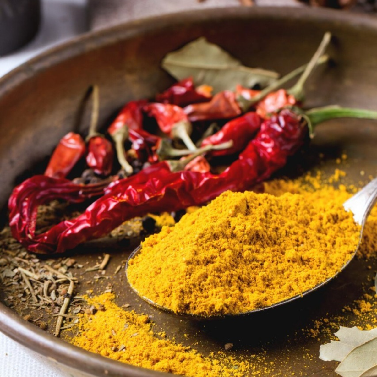 Organic turmeric powder on a spoon with dried red chilies and spices in a bowl