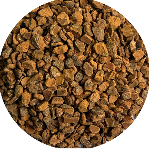 A circular close-up of small irregular brown and tan granules or chips filling the frame, shown against a black background.