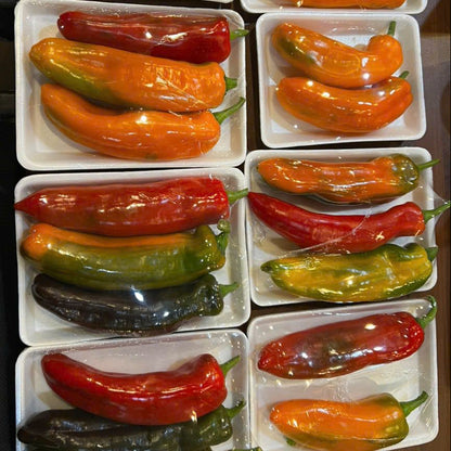 Assorted colored palermo peppers in clear plastic packaging on a wooden surface