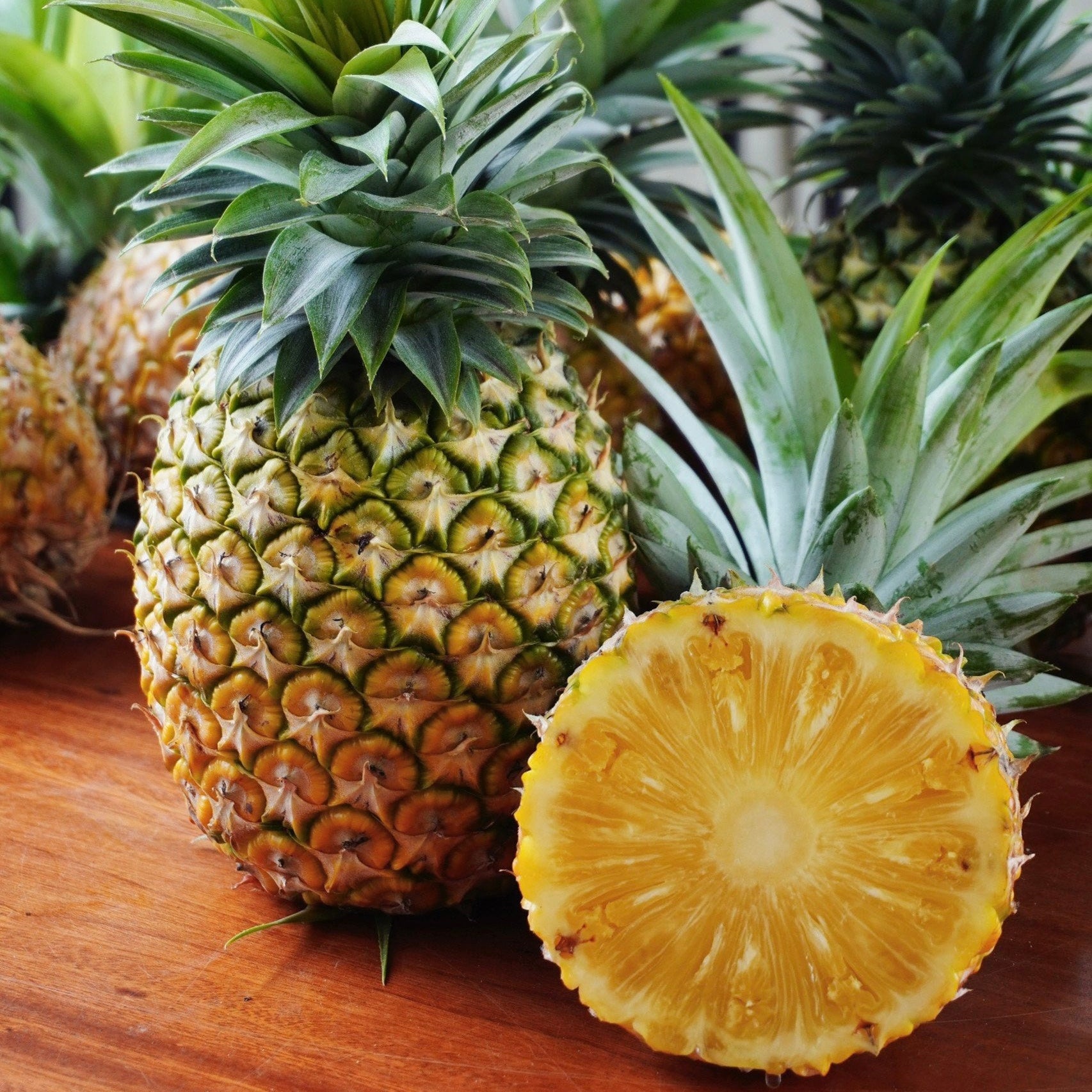 Pineapples on a wooden surface with one cut open to reveal its interior.